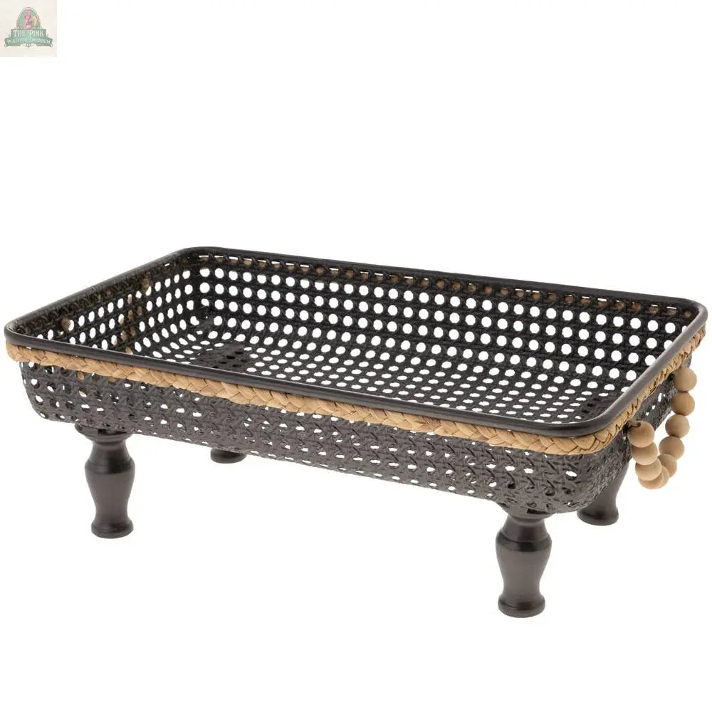 The 17" Long Rectangle Black Metal Leg Basket features black woven sides with beige trim, four short metal legs, and decorative wooden beads on one corner, adding stylish charm to any space.