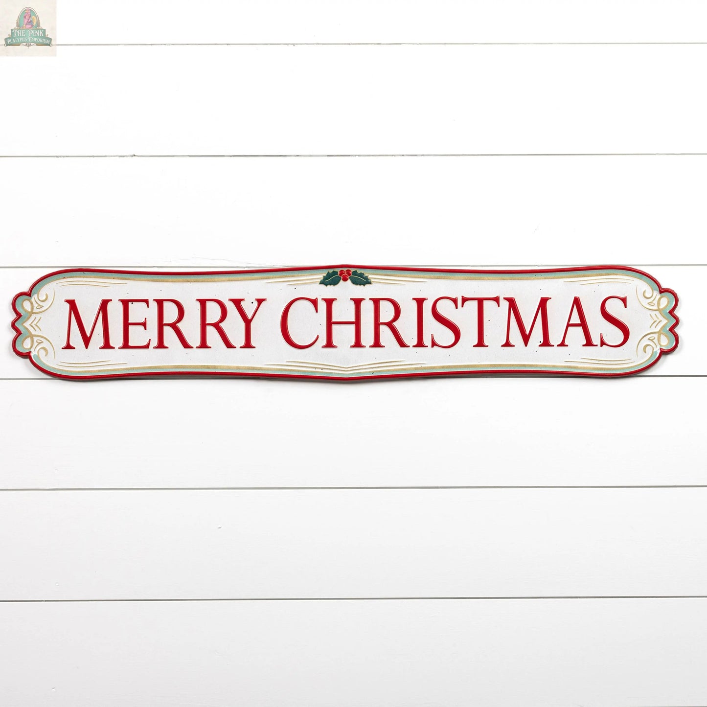 The 40" Red & White Merry Christmas Plaque features bold red letters with holly accents on a white background and gold border, mounted on a white wooden wall—ideal for festive holiday décor.