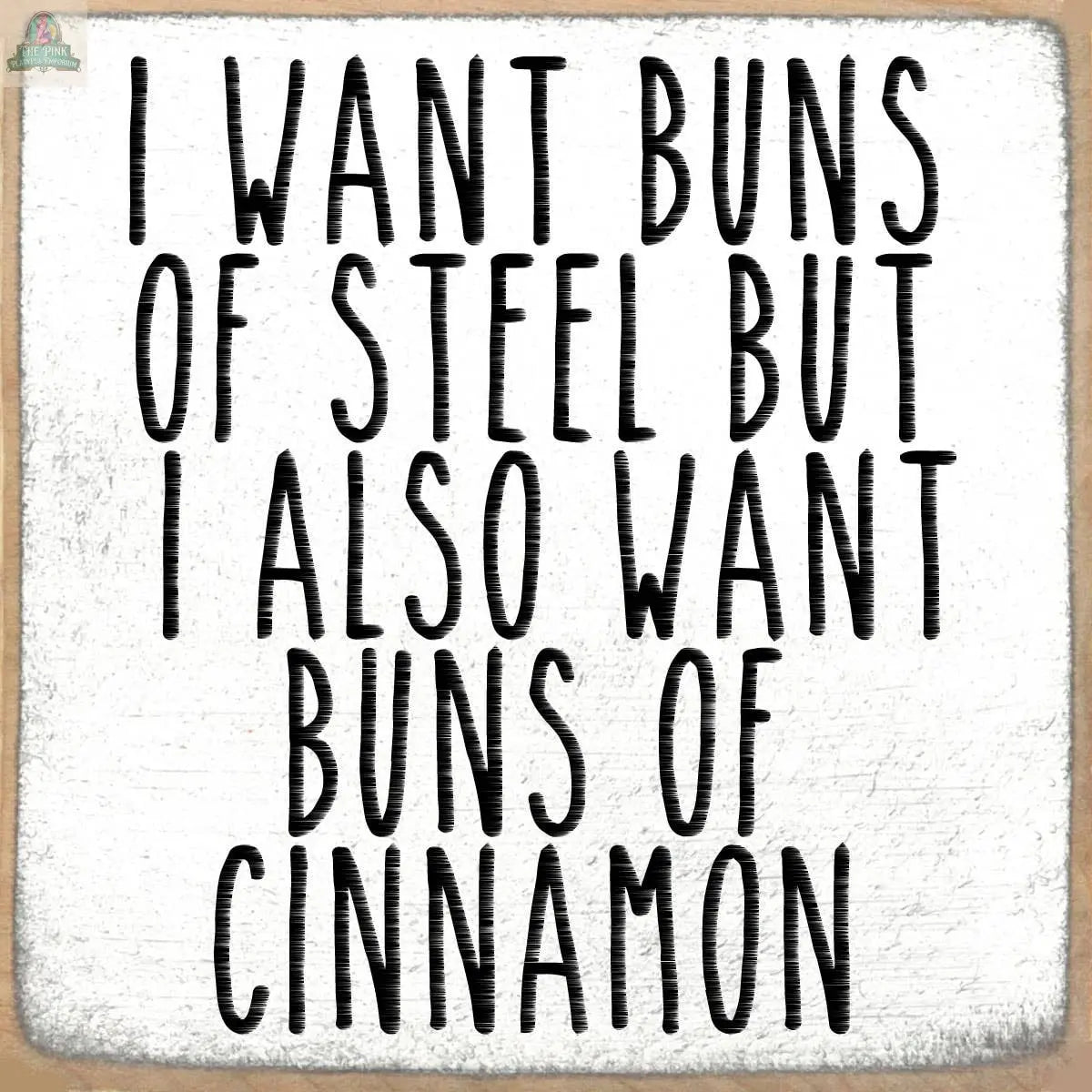 Text on a textured white background reads: I want buns of steel but I also want buns of cinnamon, in large, bold, black letters—featured on the 4X4-Cinnamon wooden block sign by Pink Platypus Emporium. Perfect for your kitchen or gym.