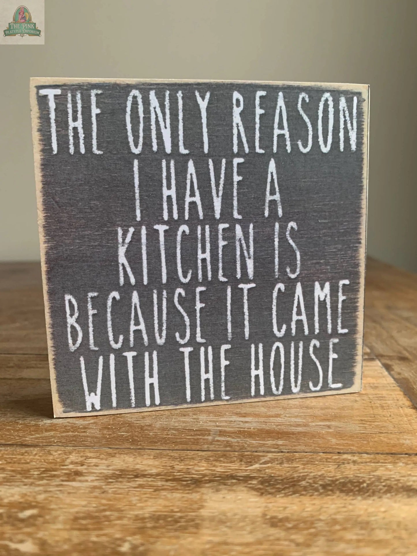 The Pink Platypus Emporium 4X4-Came with House wooden block sign features the witty phrase, "The only reason I have a kitchen is because it came with the house," making it a fun touch for your home decor.