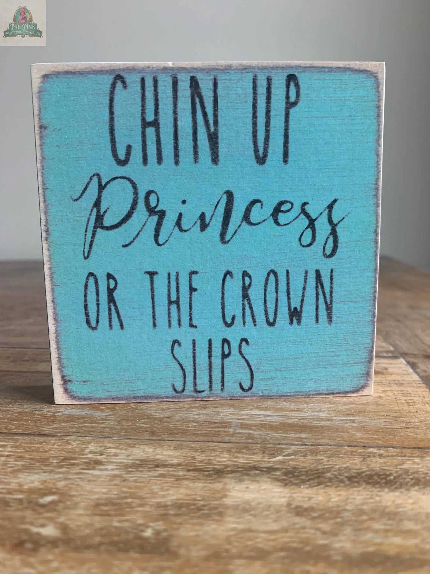 The Pink Platypus Emporium 4X4-Chin Up Princess block sign features distressed turquoise wood and black handwritten lettering, reading "Chin up Princess or the crown slips"—a perfect touch for home decor or seasonal displays.