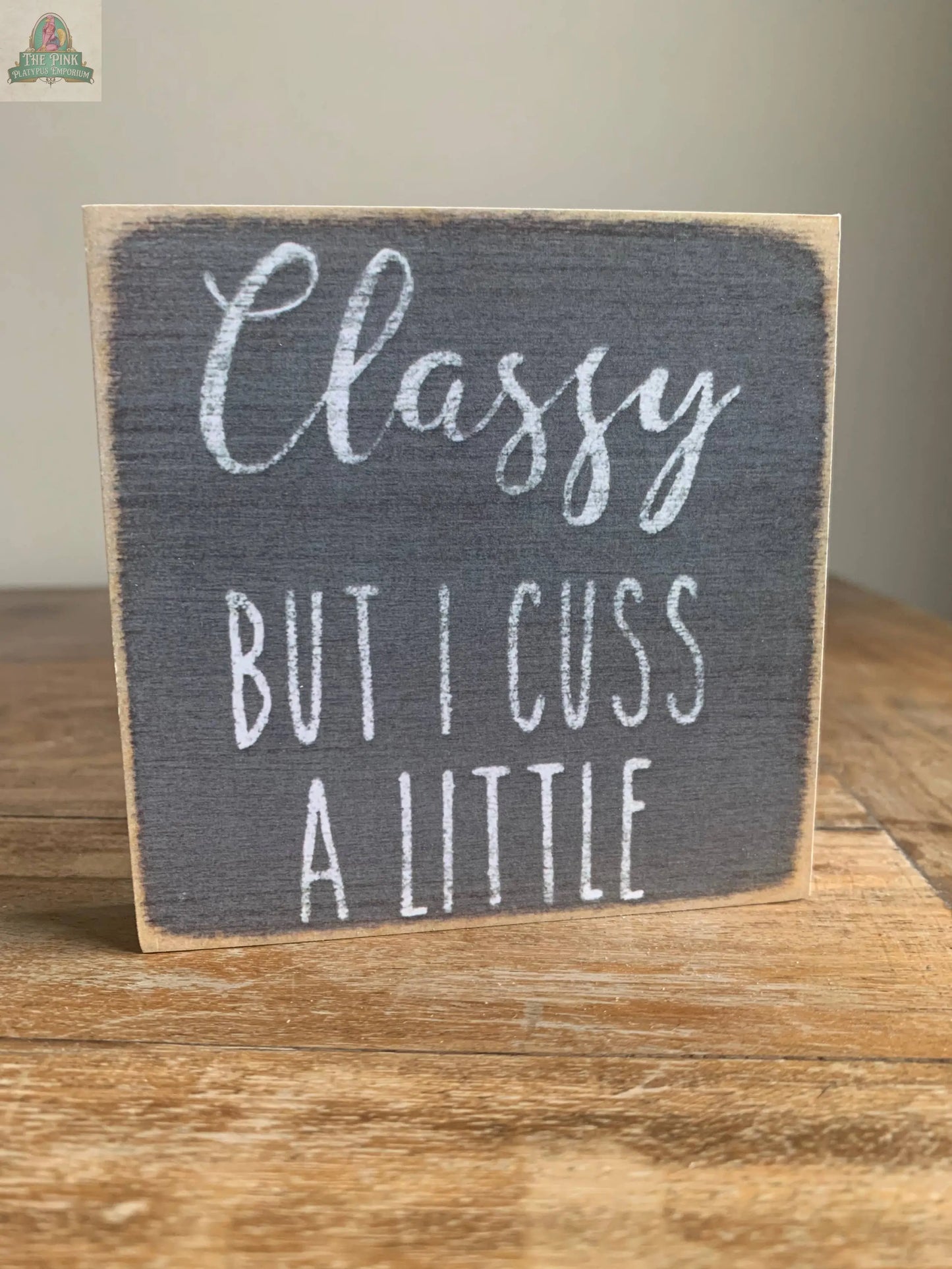The Pink Platypus Emporium 4X4-Classy Cuss is a wooden block sign featuring “Classy but I cuss a little” in white lettering—a playful and stylish accent for your home decor.