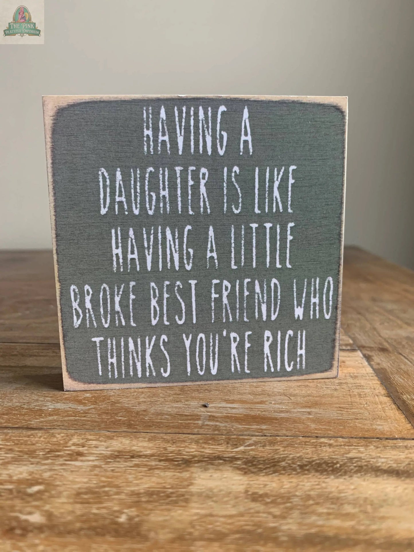 The Pink Platypus Emporium 4X4-Daughter Best Friend wooden block sign features white, handwritten-style text: "Having a daughter is like having a little broke best friend who thinks you’re rich," ideal for home decor.