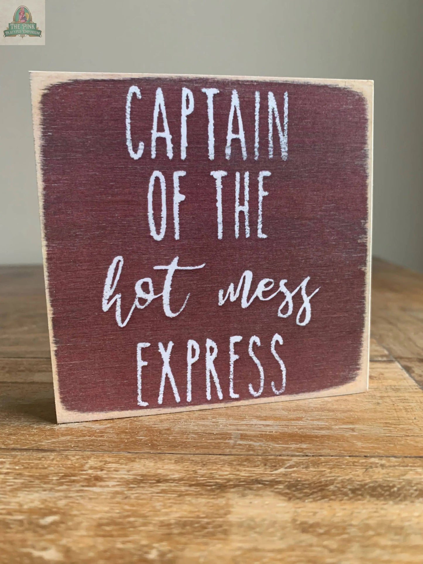 The Pink Platypus Emporium 4X4-Hot Mess wooden block sign features a maroon background with white "Captain of the hot mess express" text—perfect for bringing humor to your home decor. It’s shown resting on a wooden surface.