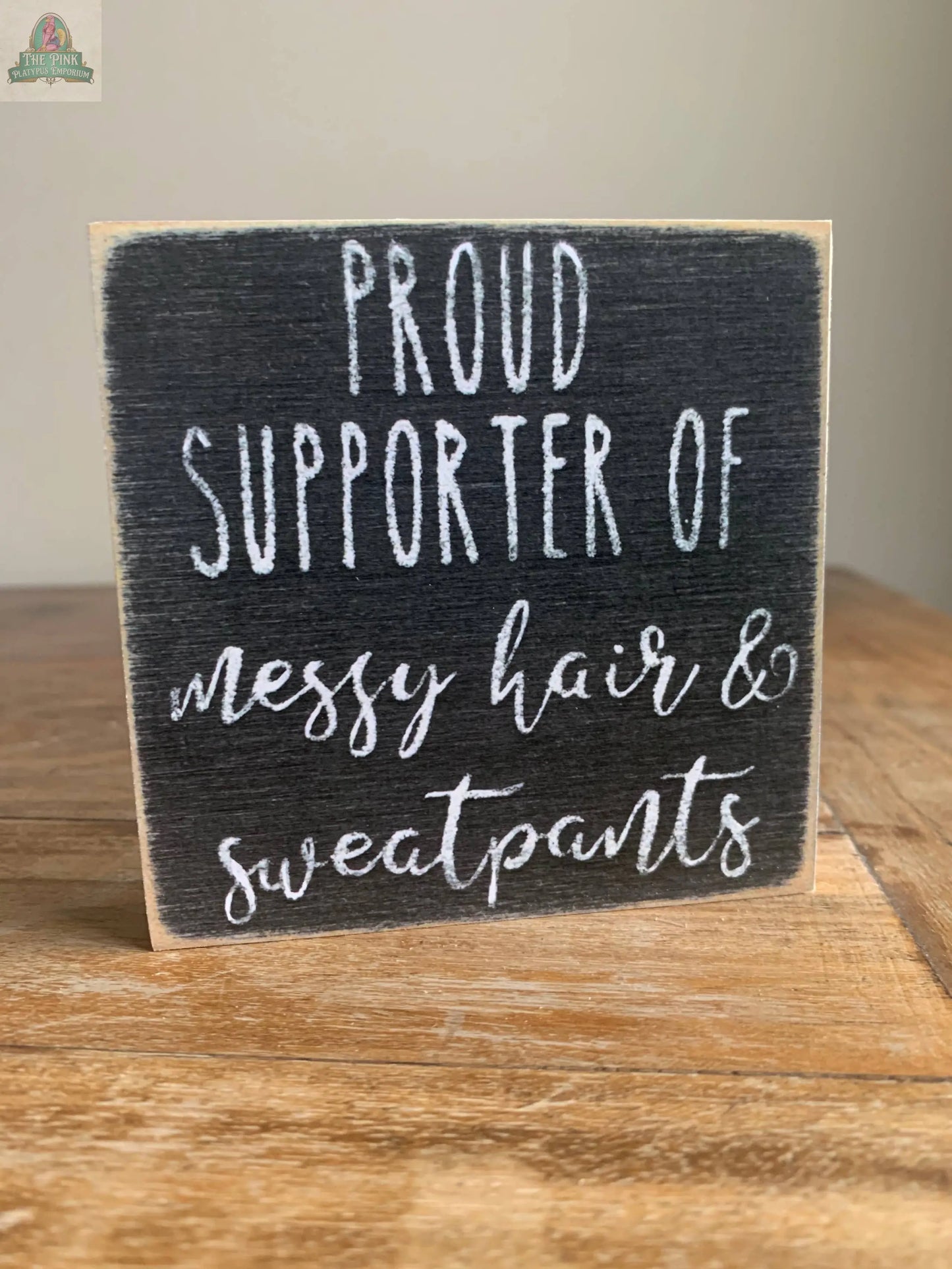The Pink Platypus Emporium 4X4-Messy Hair wooden block sign, featuring white handwritten-style text on a dark background, reads "Proud supporter of messy hair & sweatpants" and adds charm to your home decor.