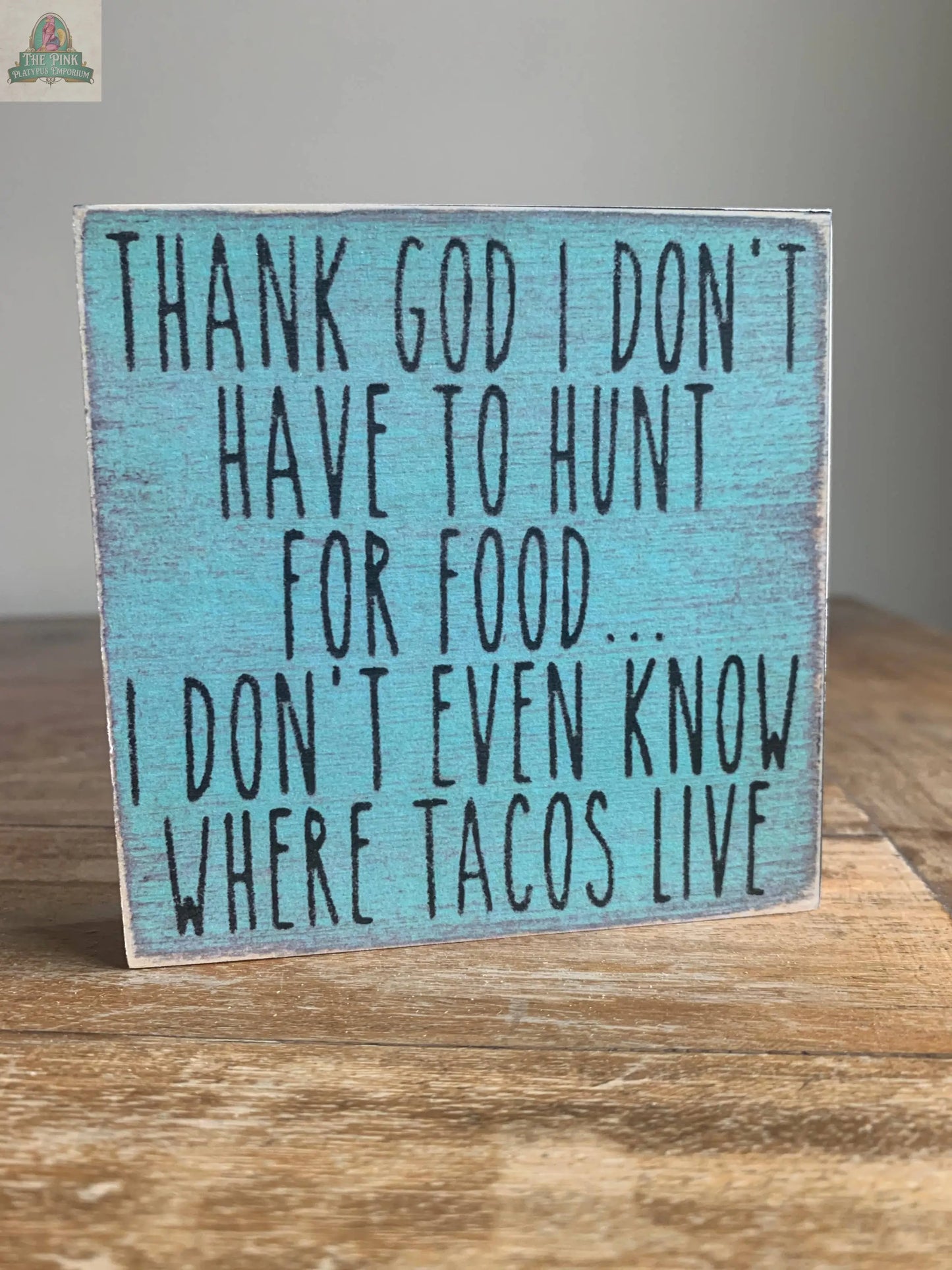 The Pink Platypus Emporium 4X4-Where Tacos Live wooden block sign, featuring a distressed blue finish and humorous taco-themed text, adds a playful touch to your home decor and can be displayed on any wooden surface.