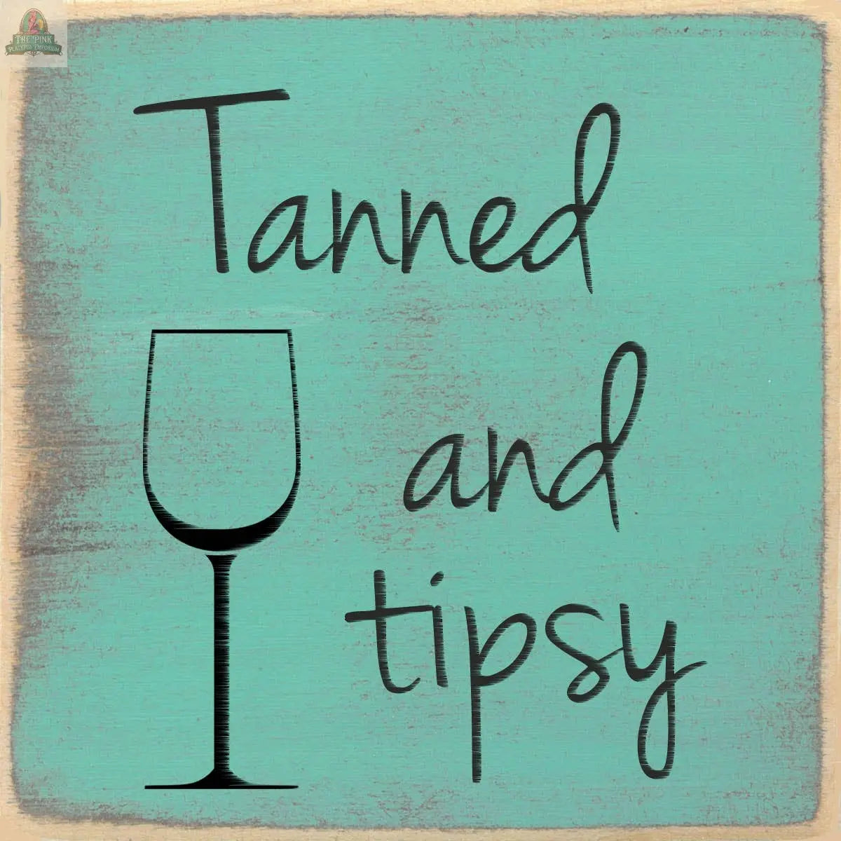 The Pink Platypus Emporium 4X4-Tanned and Tipsy wood sign features distressed teal edges, the phrase "Tanned and tipsy," and a wine glass outline for the "d," adding a charming accent to any space.