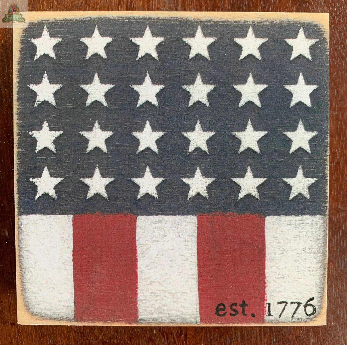 The Est 1776 Wood Sign by Pink Platypus Emporium features a stylized American flag with white stars, red and white stripes, and "est. 1776" text—ideal rustic wall decor for patriotic homes.