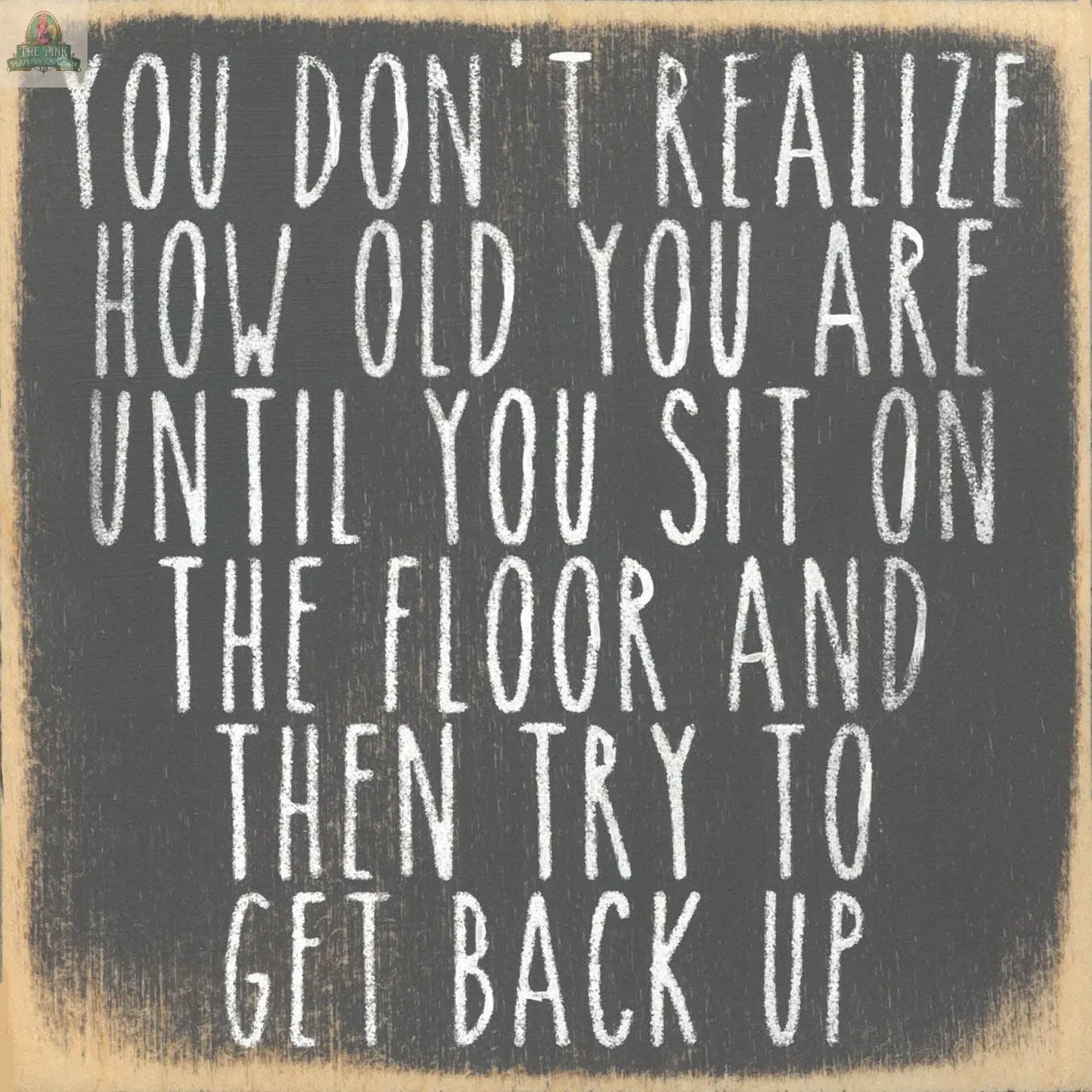 The Get Back Up Wooden Sign by Pink Platypus Emporium features playful chalkboard-style text: "You don't realize how old you are until you sit on the floor and then try to get back up"—a fun, inspirational home decor piece.