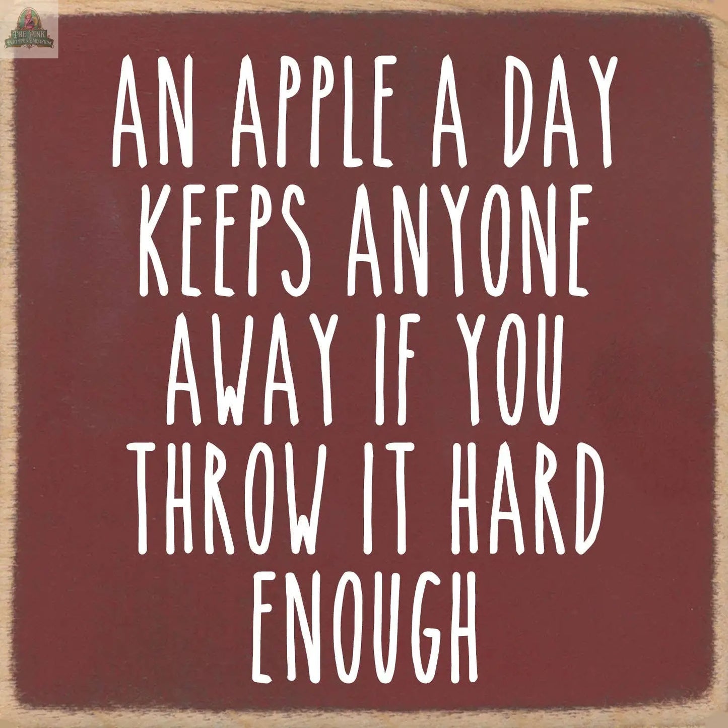 The Pink Platypus Emporium 5X5-An Apple wooden sign features white text on a brown background: "An apple a day keeps anyone away if you throw it hard enough"—a playful accent for your home decor.