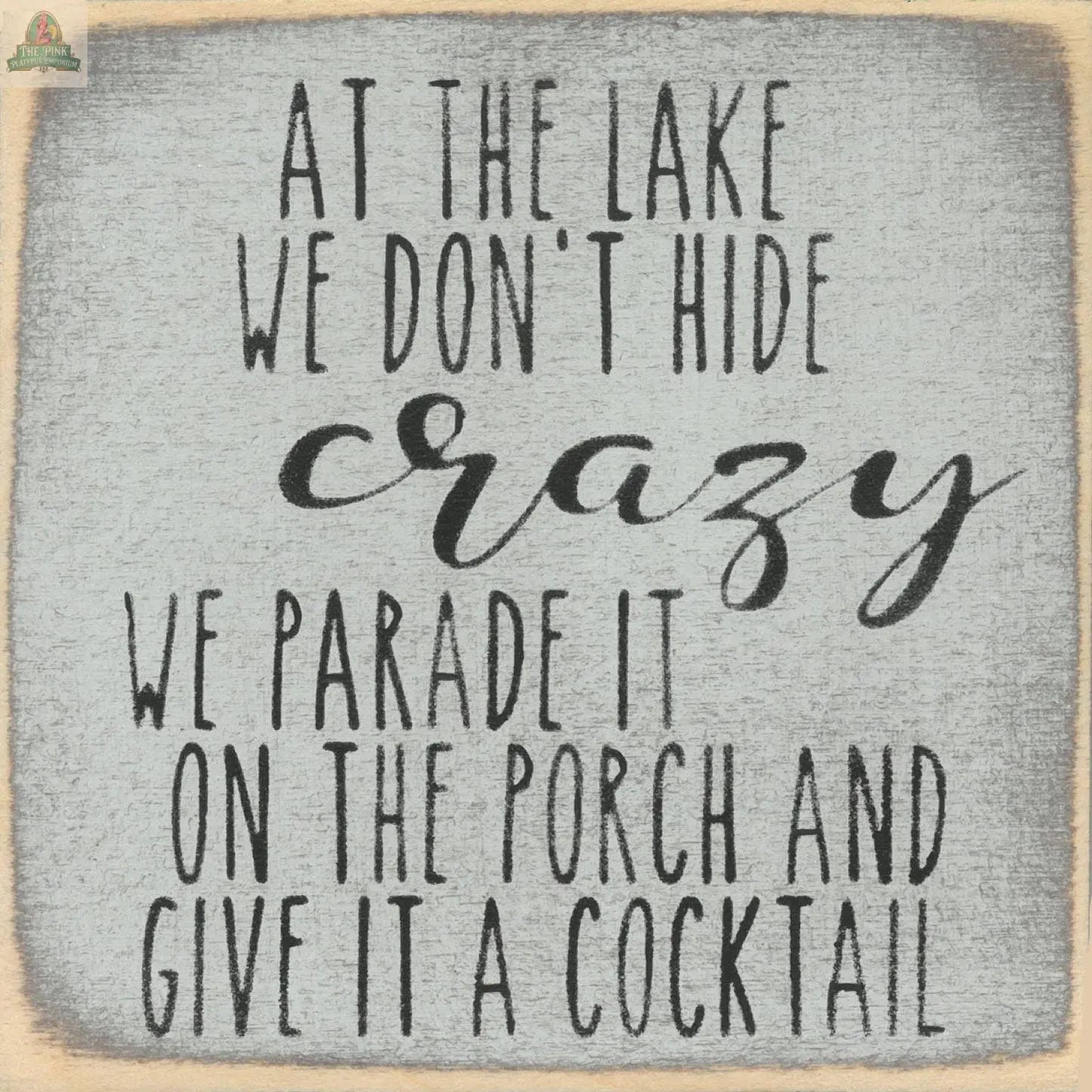 The Pink Platypus Emporium "Don't Hide Crazy" wooden block sign features playful lettering: At the lake we don't hide crazy, we parade it on the porch and give it a cocktail—perfect for adding humor to your decor.