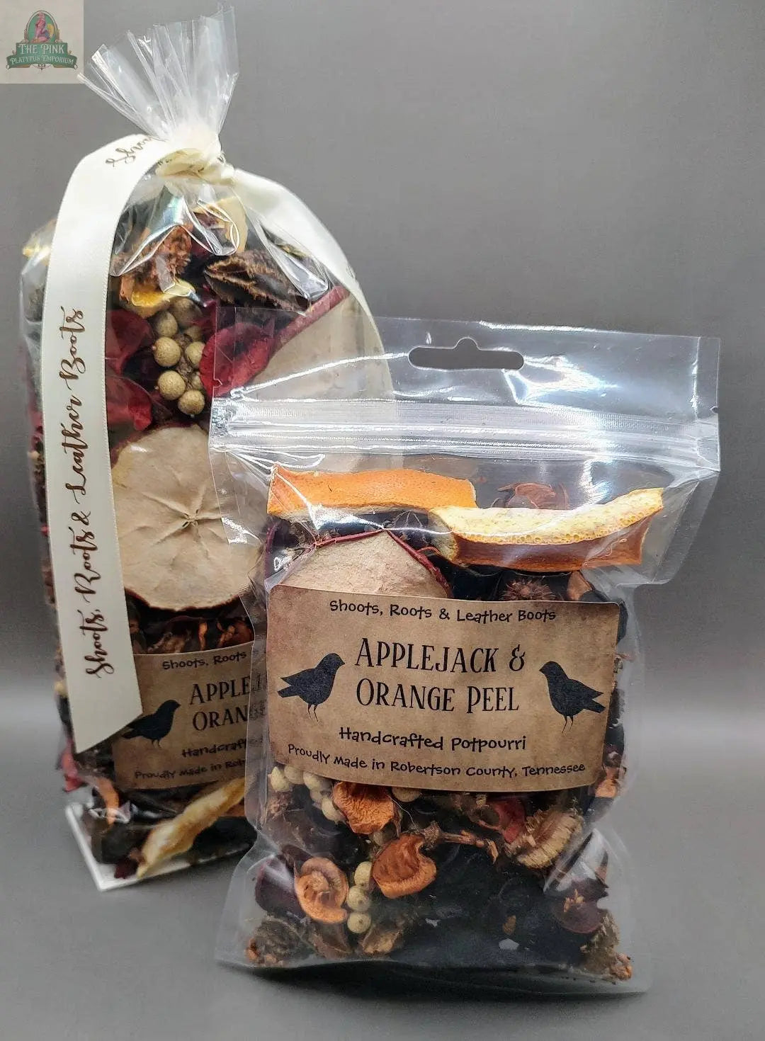 Two clear bags of Applejack & Orange Peel Handcrafted Potpourri (5 cups), filled with dried fruit and botanicals. Packaging features rustic labels, blackbird graphics, and provides an eco-friendly home fragrance.