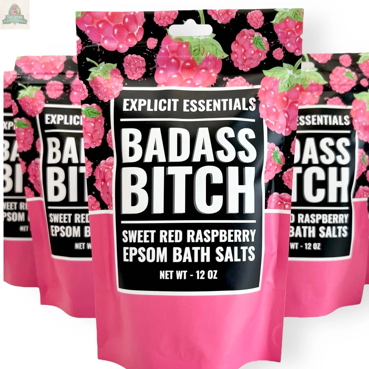 The Explicit Essentials Bad Ass Bitch Bath Salts 12oz Bag features a bold black-and-pink pouch with raspberry illustrations—an eye-catching self-care gift. Multiple pouches are shown, each labeled with the brand at the top.