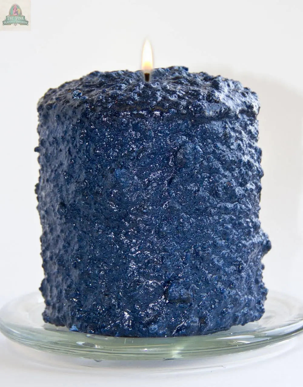 The Blueberry Cobbler Hearth Candle by Pink Platypus Emporium sits on a glass plate, infusing any space with handmade charm and a sweet blueberry aroma.