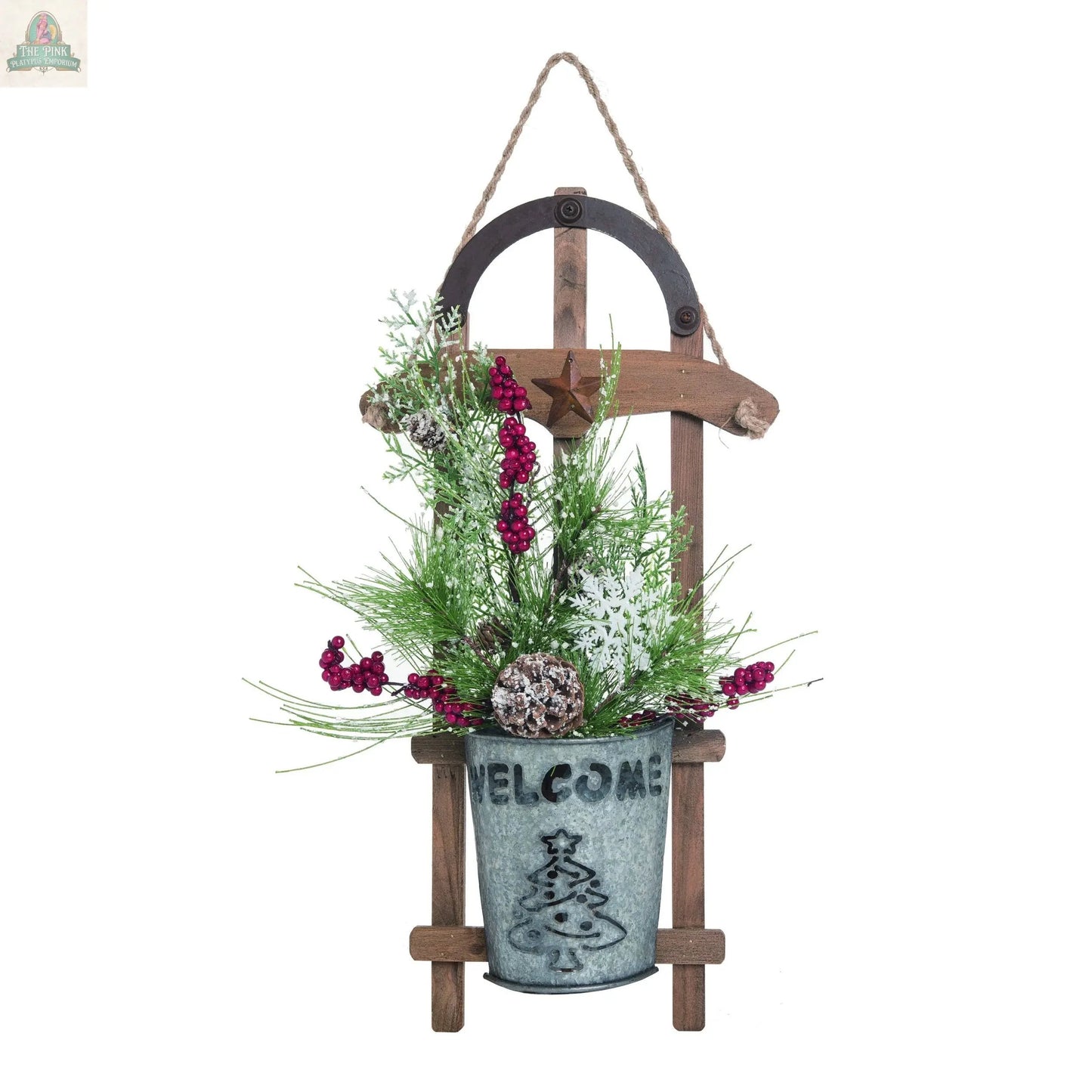 The 20" Wood Sled Ornament Christmas Decor wall hanging features a metal bucket with WELCOME and tree design, filled with pine branches, red berries, white flowers, and a pine cone. A rope loop at the top makes it great for holiday display.