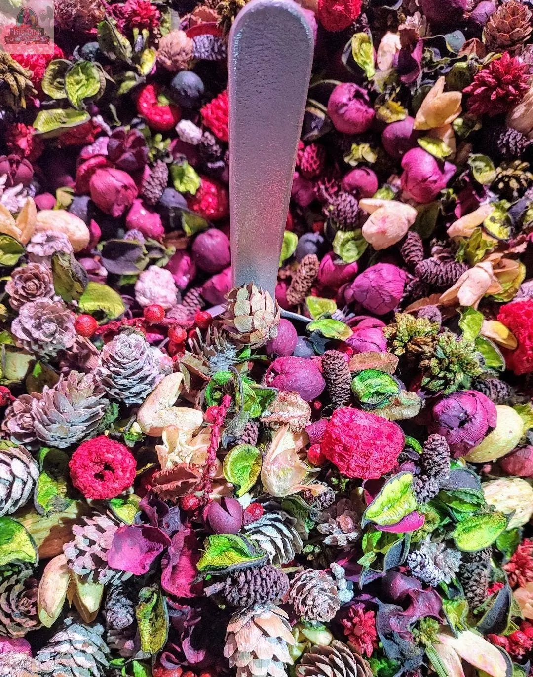 A close-up of Candy Cane Handcrafted Potpourri (5 cups), ideal as a scented bowl filler, featuring dried pine cones, berries, petals, and leaves in festive red, purple, green, and cream hues. A silver scoop rests at the center.