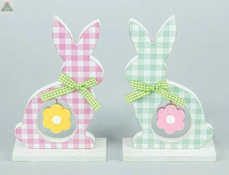 The Checkered Cottontail with Flower Tabletop 2 Assorted features one pink and one green bunny figurine with bows and flower cutouts, standing on white bases. Ideal for spring décor or farmhouse Easter decorations.