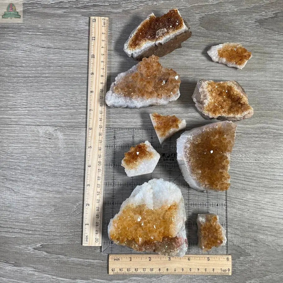 Several Keystone Crystals Citrine Crystal Clusters – Natural Golden Gemstone Décor from Pink Platypus Emporium are arranged on a gray wooden surface, with three rulers for scale, showcasing the vibrant energy of the Stone of Abundance.