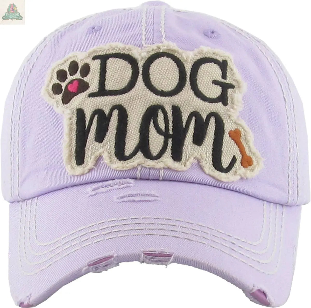 The Pink Platypus Emporium DOG MOM WASHED VINTAGE BALLCAP: DBL is a light purple women’s hat with distressed details, a “Dog Mom” patch in black, a paw print with a pink heart, and a small brown bone—perfect for stylish dog moms.