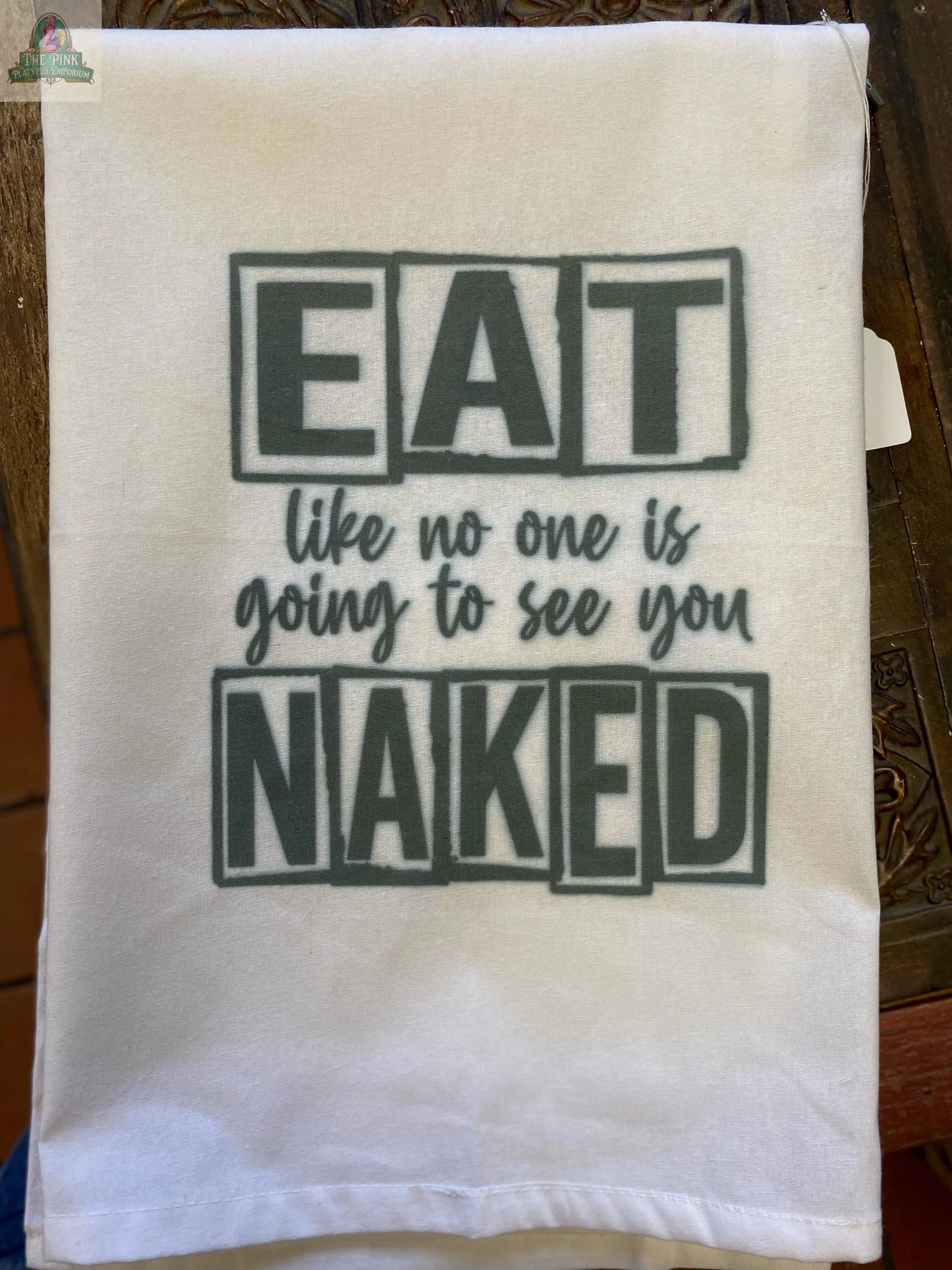Add humor to your kitchen with the Pink Platypus Emporium Funny Tea Towel: "Eat like no one is going to see you Naked"—bold black text with EAT and NAKED boxed for emphasis makes this a standout decorative towel for any home.