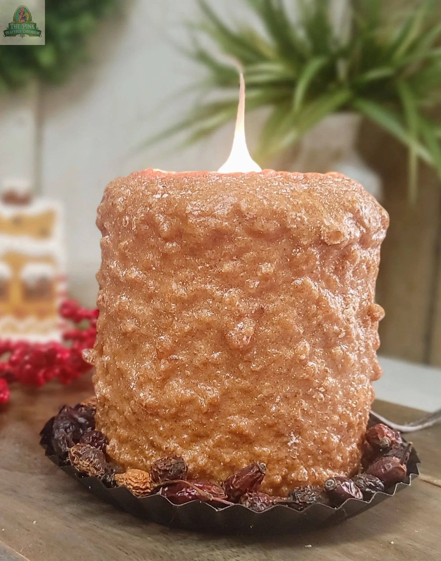 A handmade Gingerbread Cookie Electric Candle, textured and brown, sits on a dark tart pan with dried berries, while festive greenery and decorations blur in the background. Crafted in the USA and shaped like a baked dessert.