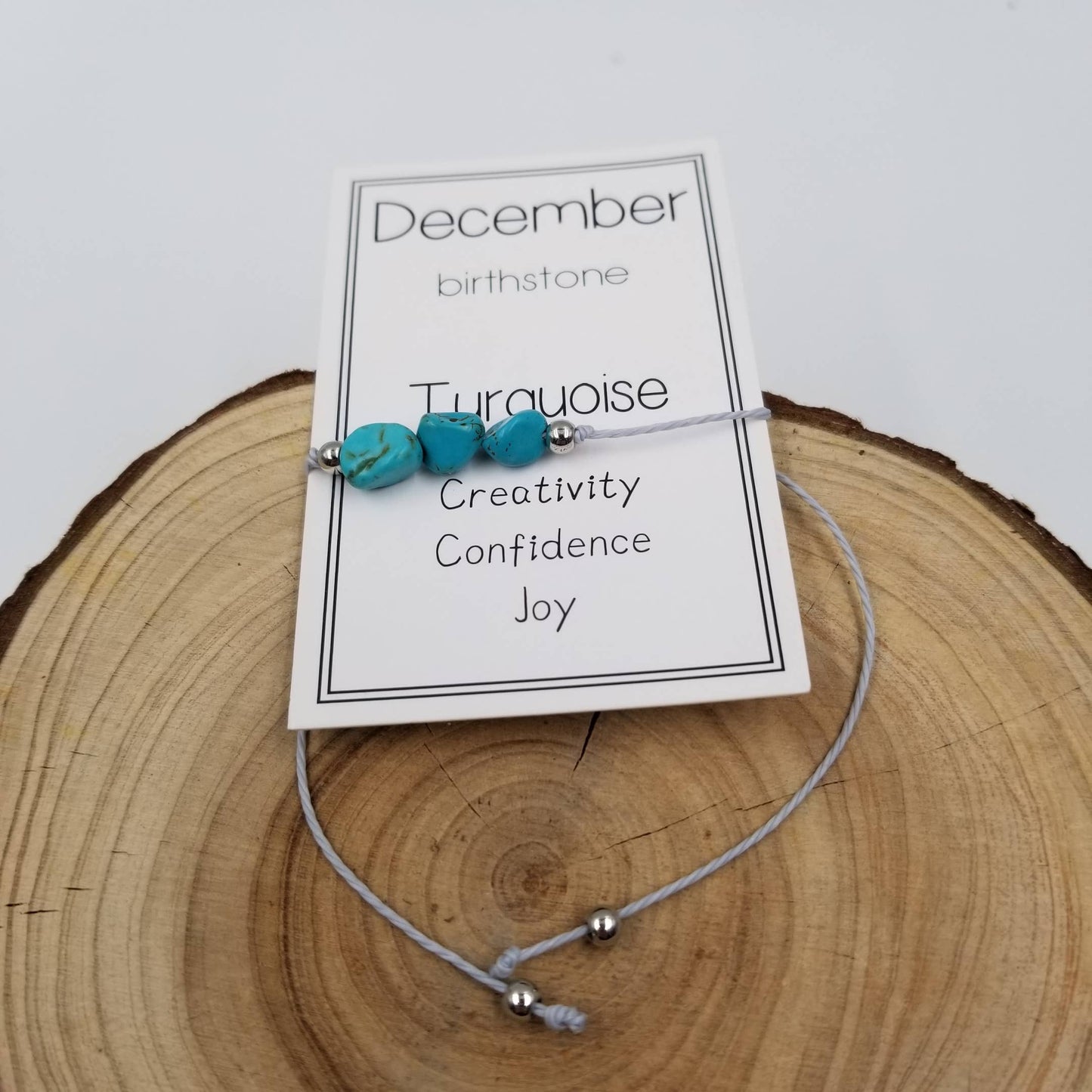 The Pink Platypus Emporium Handmade Birthday Stone Natural Stone Bracelet with Card: August is shown atop a wooden surface, featuring a card reading August birthstone—ideal as a unique birthday stone bracelet gift.