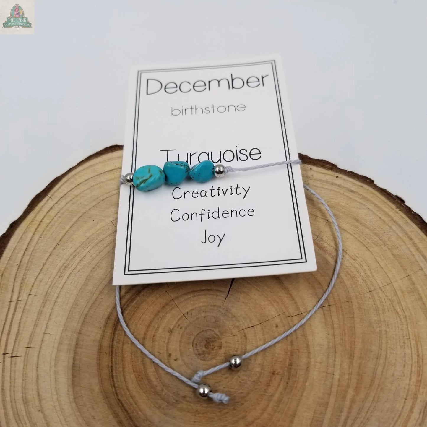 The Pink Platypus Emporium Handmade Birthday Stone Natural Stone Bracelet with Card: October features a bracelet displayed on a card labeled October birthstone, listing stone details and descriptors, all resting on a wooden surface.