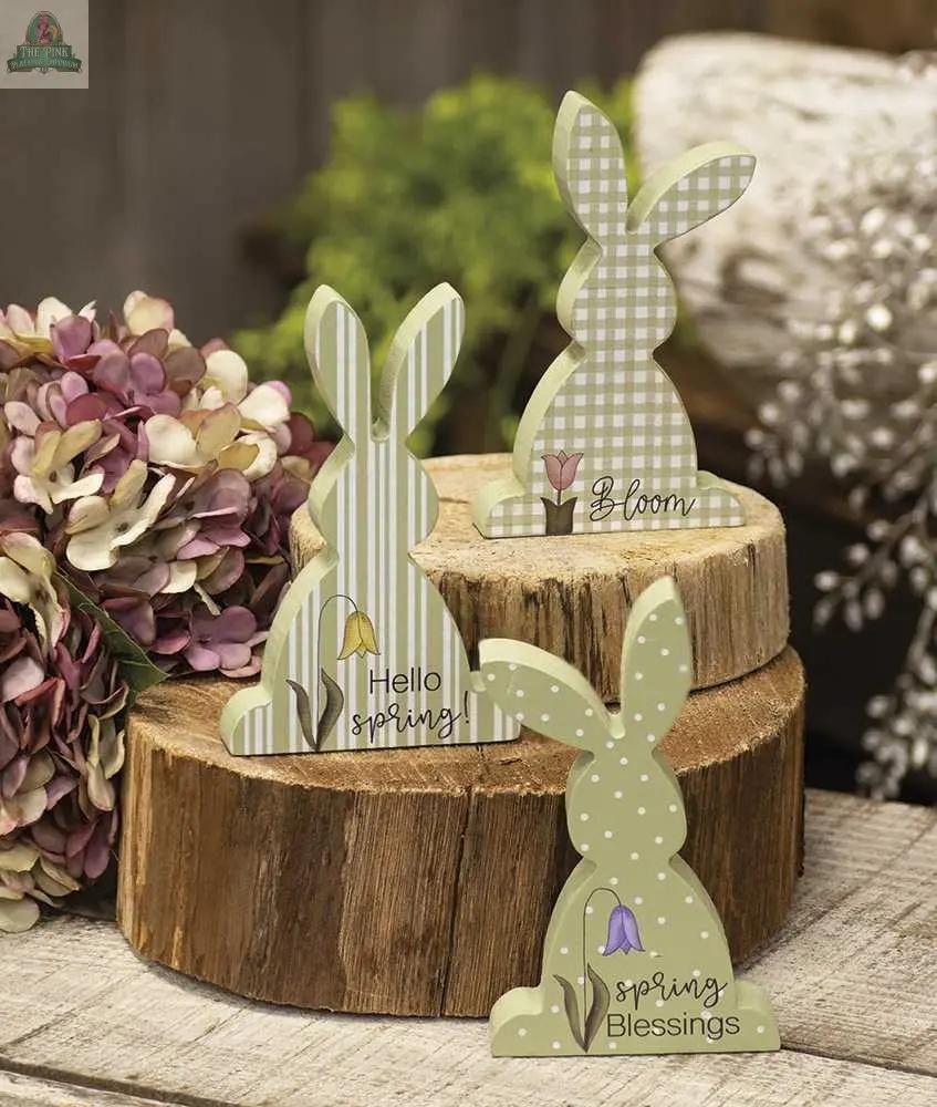 The Hello Spring Chunky Bunny, 3 Assorted features decorative bunnies with spring patterns and words, displayed on stacked wood rounds with dried hydrangeas—ideal for charming seasonal decor.
