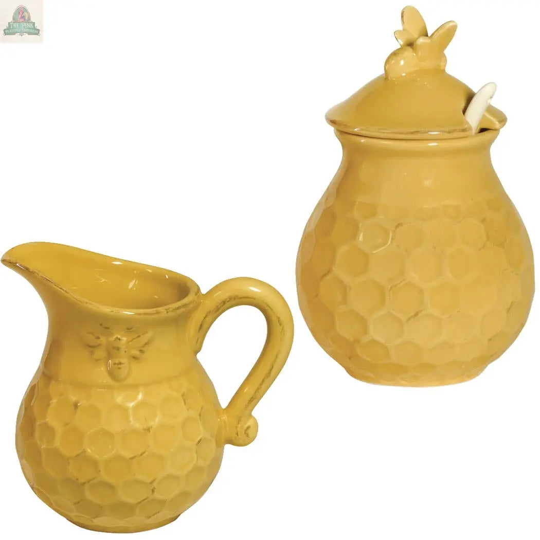 The Pink Platypus Emporium Honeycomb Ceramic Cream & Sugar Set includes a yellow pitcher and honey jar with lid and spoon, both featuring a bee and honeycomb design. Microwave and dishwasher safe for convenience.