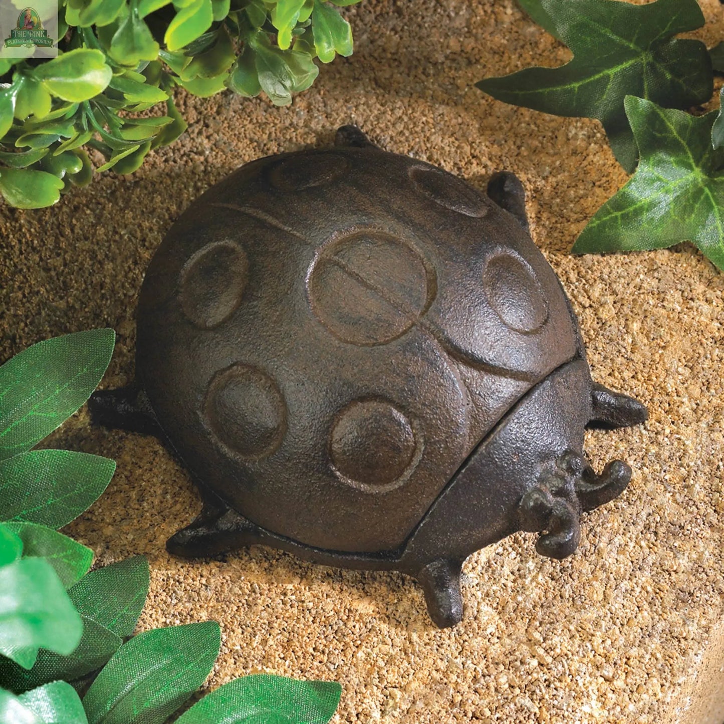 The Ladybug Key Hider features a metal, textured surface with circular spots and blends into garden foliage, making it an ideal and whimsical way to keep your spare key hidden outdoors.