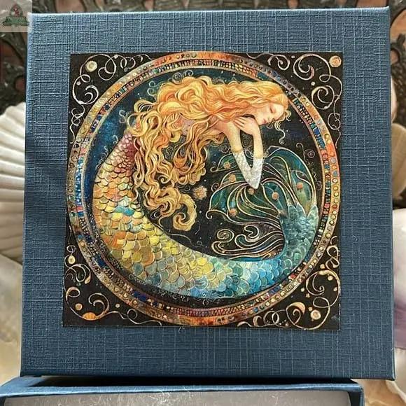 A vibrant illustration of a mermaid with golden hair, surrounded by swirling patterns and hag stones, features on the Mermaid Keychain Gift Set with Local Hand Chosen Beach Stone.