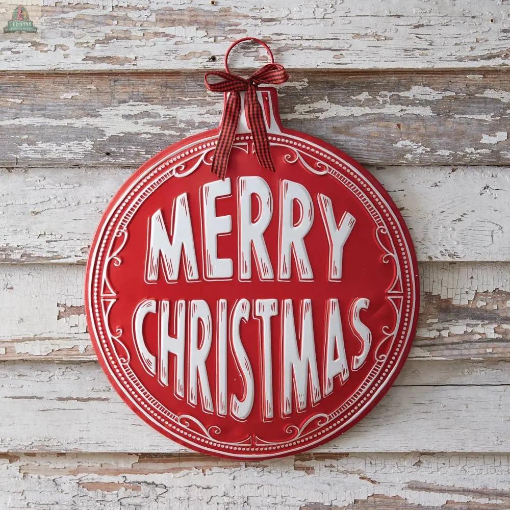 The Merry Christmas Ornament Wall Decor is a round red sign with “Merry Christmas” in large white letters, hung by a red and white checked ribbon. Ideal for holiday decorating, it adds festive charm to any rustic, white-painted wooden wall.