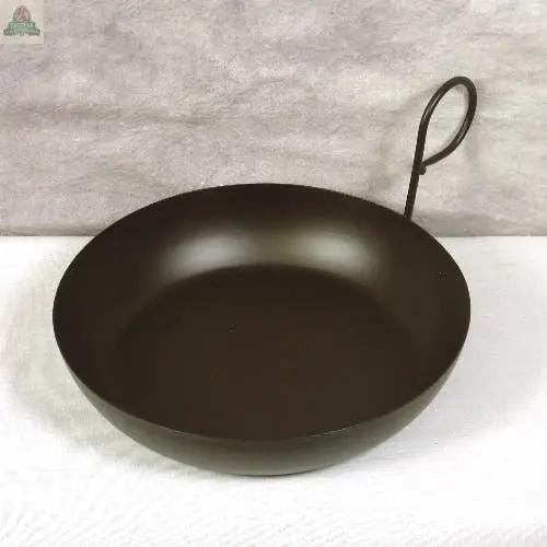 A Metal Gravy Pan candle Holder in burgundy, with a round bottom and single looped handle, sits on a white textured surface against a light gray background.