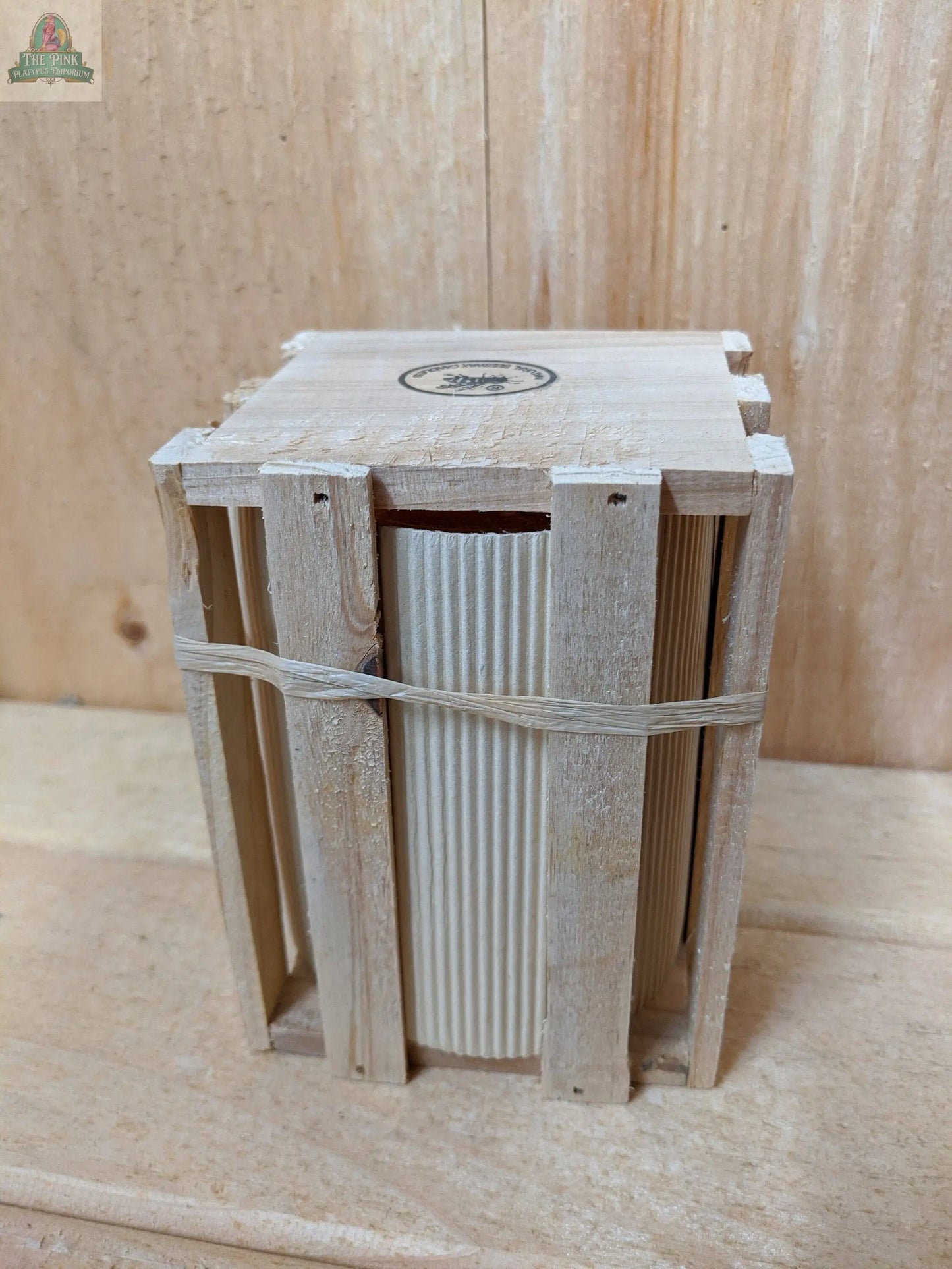 A set of Pure Beeswax Candles 34 W/Y: Yellow from Pink Platypus Emporium, wrapped in ridged paper and nestled in a small wooden crate secured with rubber bands, sits on a wooden surface—eco-friendly packaging, thoughtfully crafted.