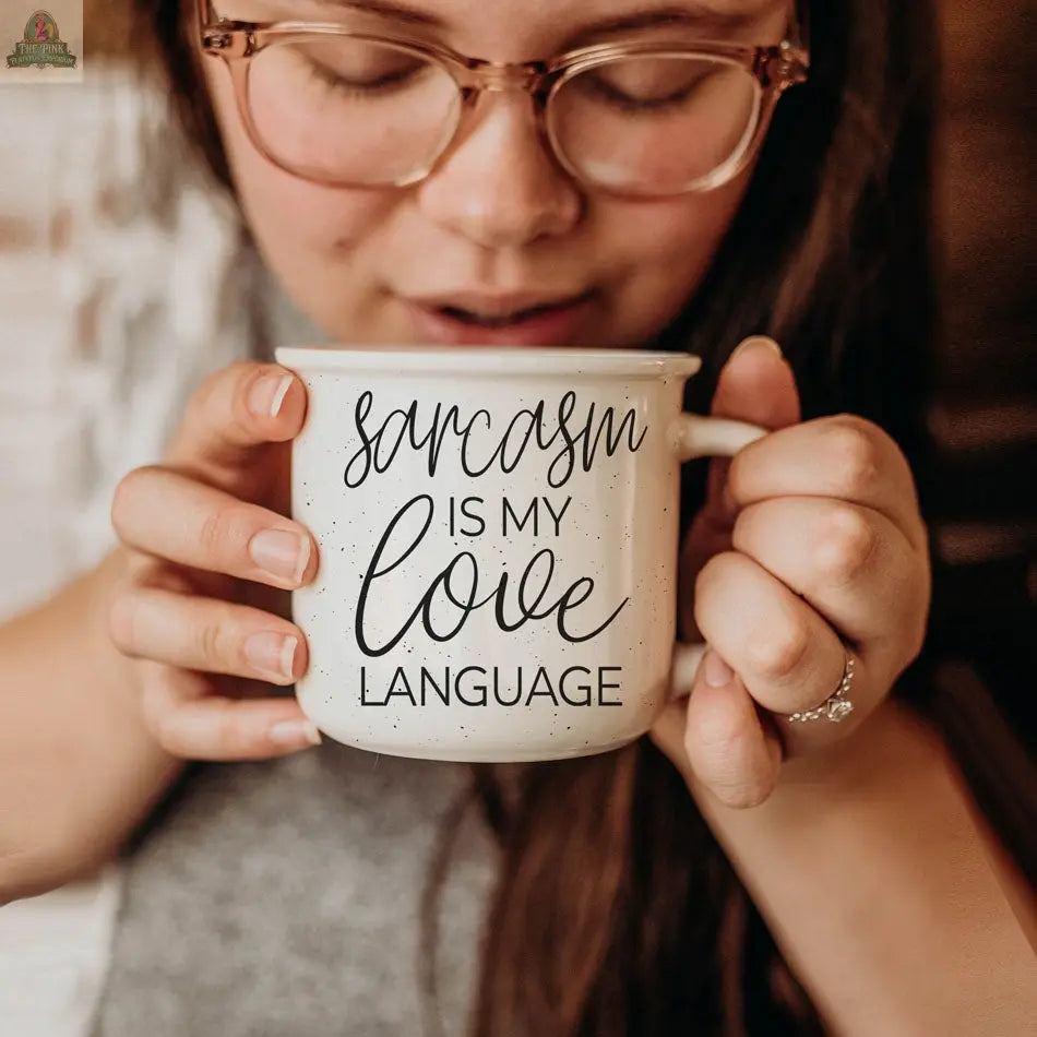 A woman with glasses gently smiles while holding the 14.5oz Sarcasm Love ceramic mug featuring the phrase "Sarcasm is my love language" in a decorative font.