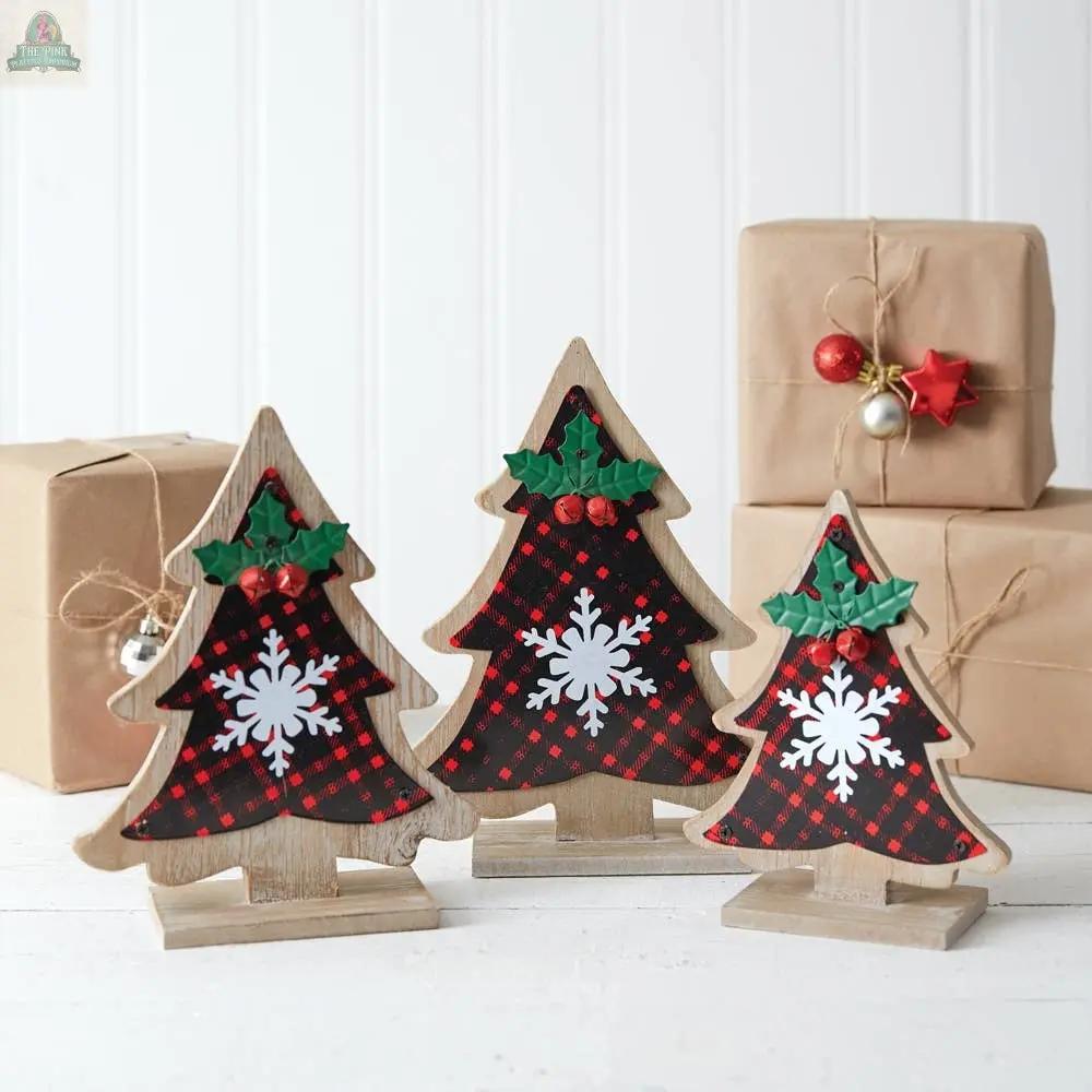 The Set of Three Buffalo Plaid Tabletop Trees, made of wood with metal accents, features holly leaves, red berries, and snowflakes. Arranged before gift boxes tied with string, they create charming Christmas decor on a white background.