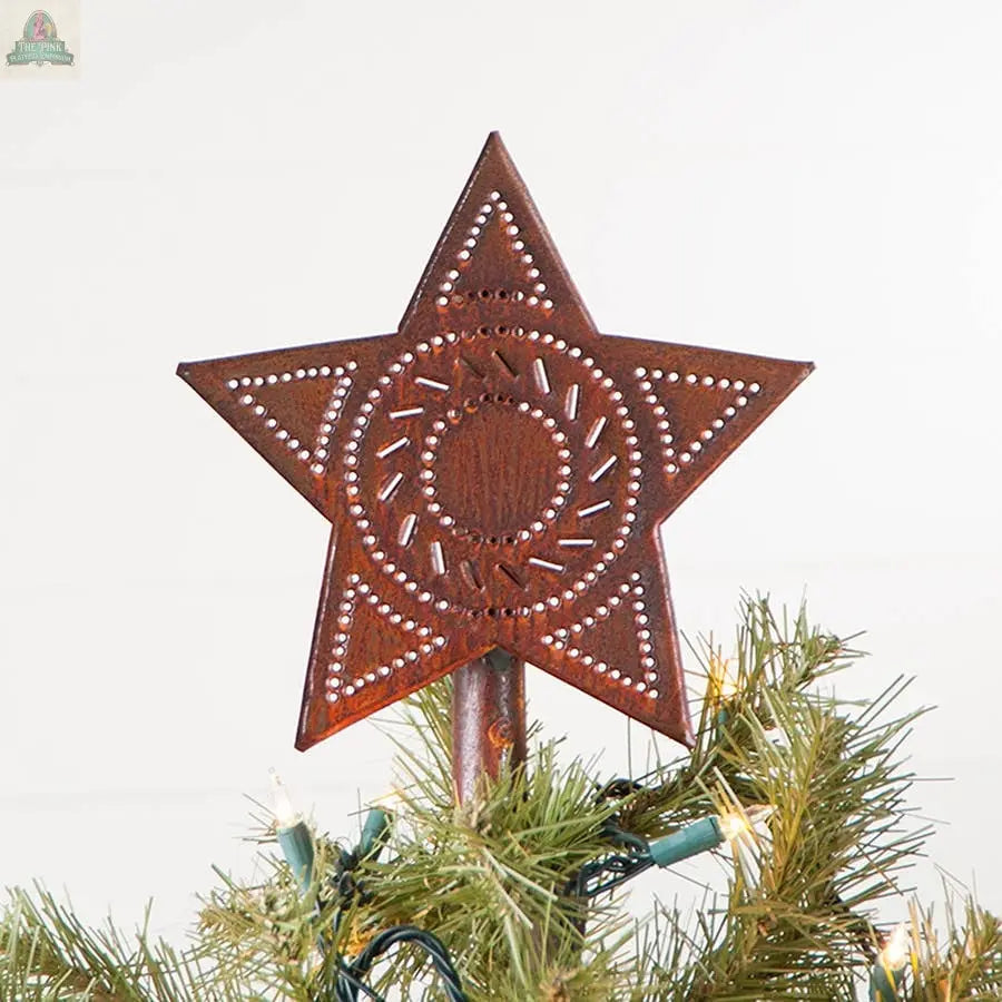 The Star Tree Topper in Rustic Tin by Pink Platypus Emporium, featuring a perforated star and circular center design, crowns a green Christmas tree decorated with string lights.