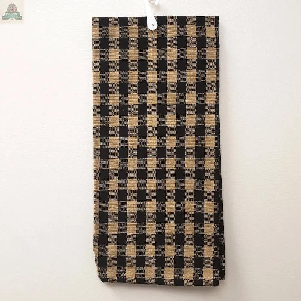 The Tan & Black Check Kitchen Towel, sized 15 x 25 inches, features a tan and black check pattern and hangs against a white wall by a white top loop.