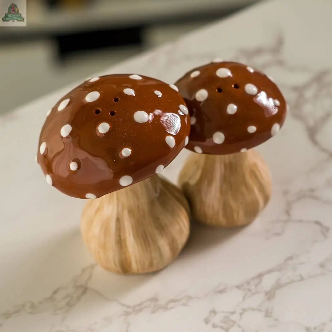 The Toadstool Mushrooms Salt and Pepper Shaker Set features two ceramic shakers with white spots and light brown stems, adding a whimsical touch to your kitchen décor.