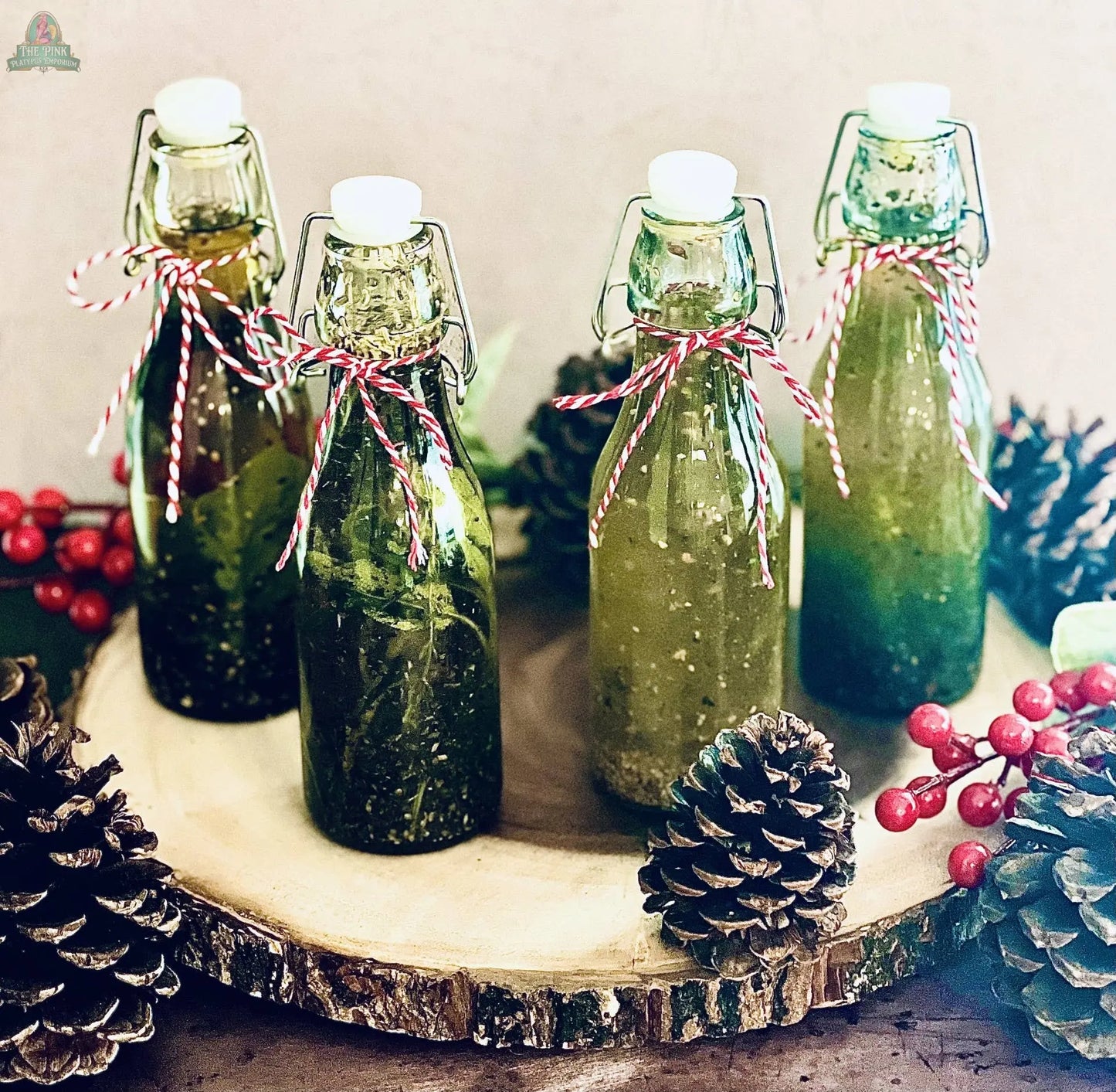 Four bottles of Carmie's Kitchen Toasted Garlic Dipping Oil Seasoning, tied with festive string, are displayed on a wooden platter with pinecones and red berries for a rustic holiday touch, ideal for your appetizer spread.