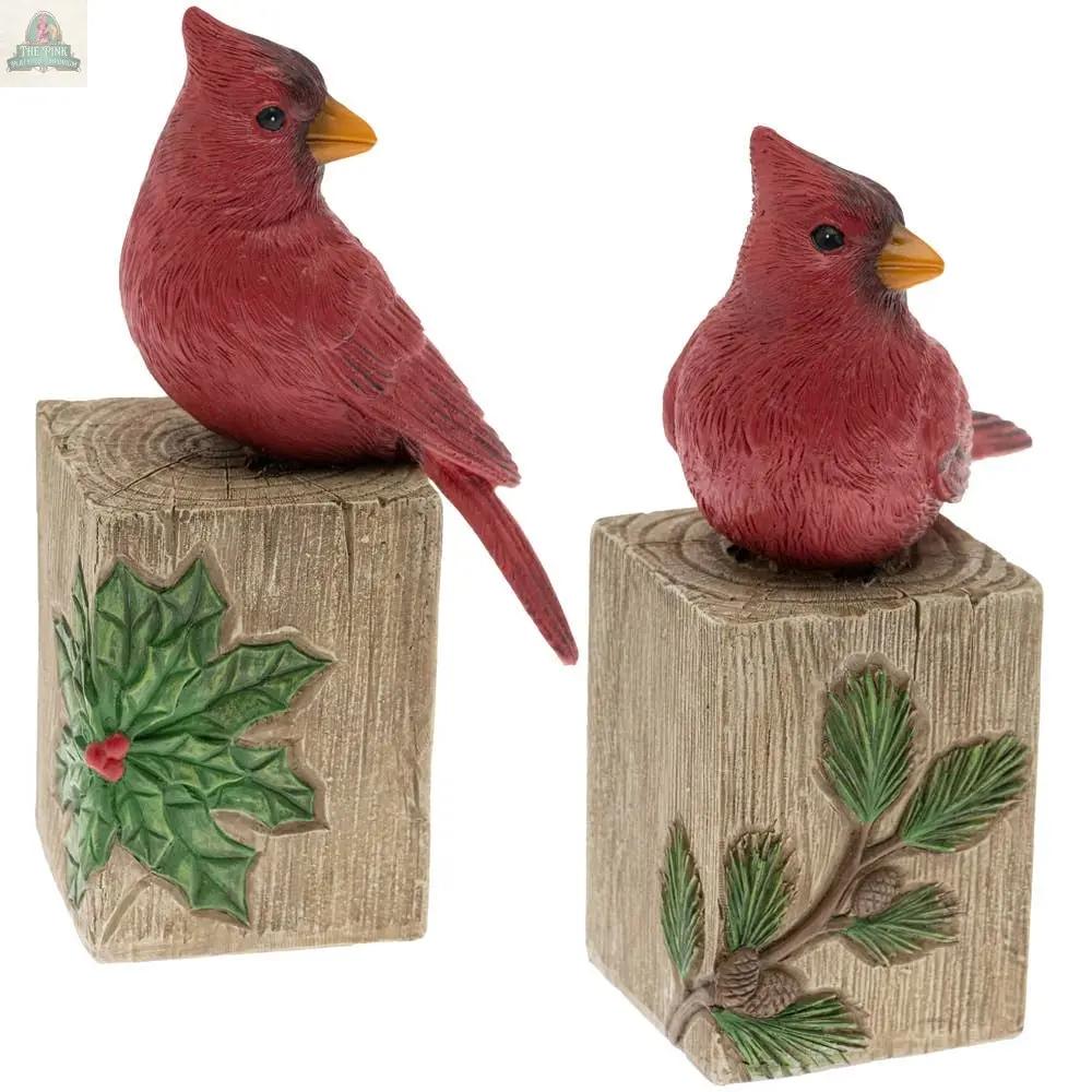 The Wood Block Cardinals Set of 2 Christmas features two resin cardinals on textured blocks—one with holly and berries, the other with pine needles and cone—perfect for festive holiday decor.