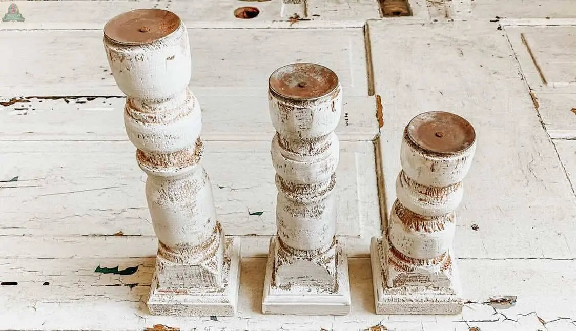 The Pink Platypus Emporium Wood Candle Holder 3 PC Set features three rustic white holders of varying heights, each with a weathered vintage finish and visible wood texture, arranged on a painted wooden surface.