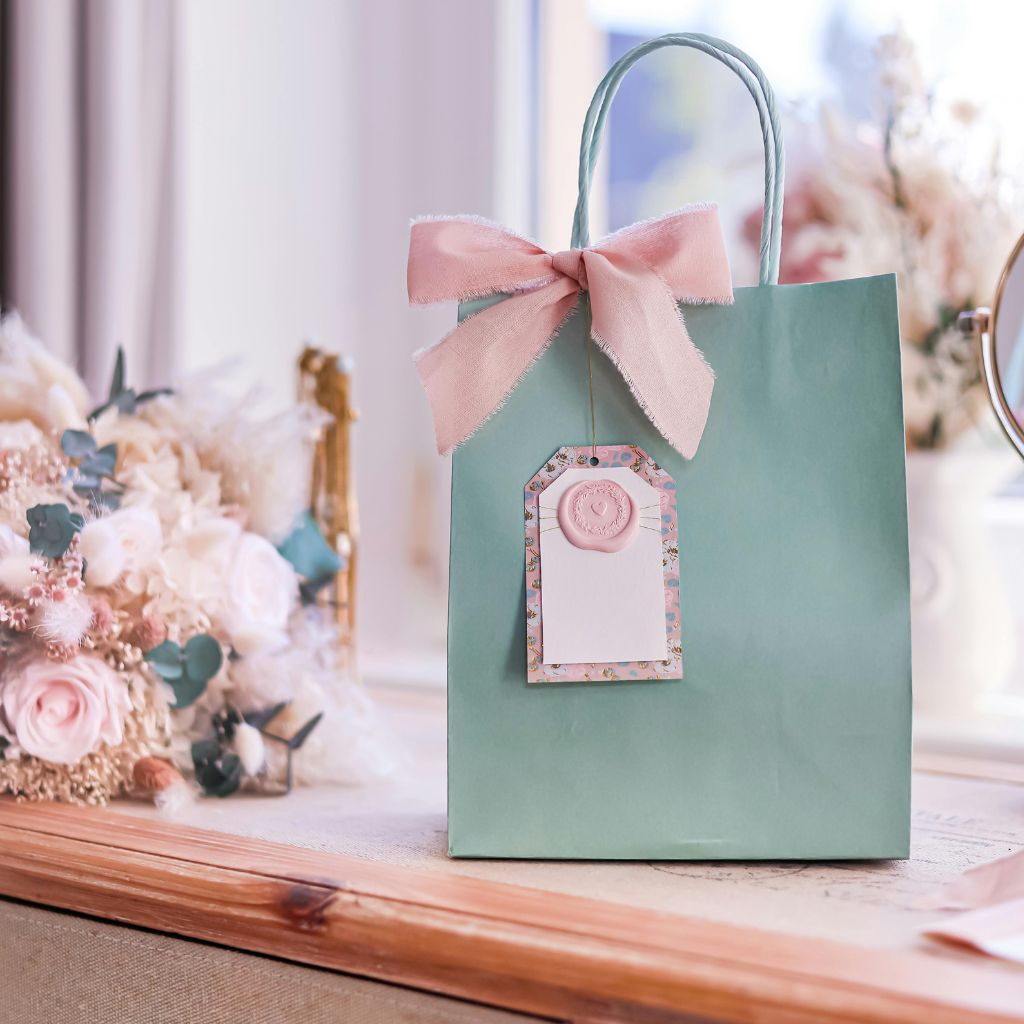 Mint green gift bag with pink bow on floral table, perfect for quirky holiday gifting and Pink Platypus Picks 2026 collection display