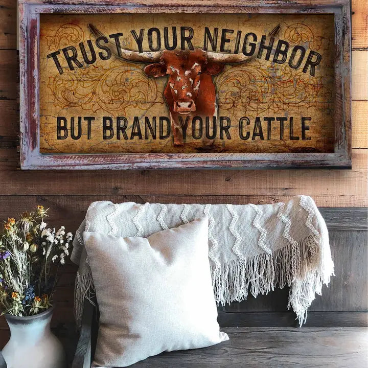 western wall decor with cow illustration and text 'Trust your neighbor but brand your cattle' above a cozy living room setting.