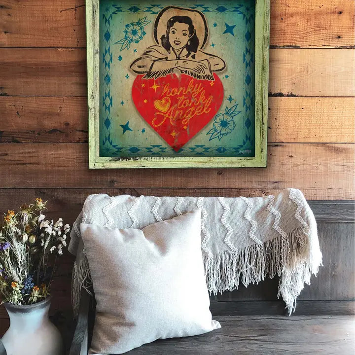 Framed artwork with a woman holding a heart and 'Honky Tonk Angel' text on a wooden wall above a couch.