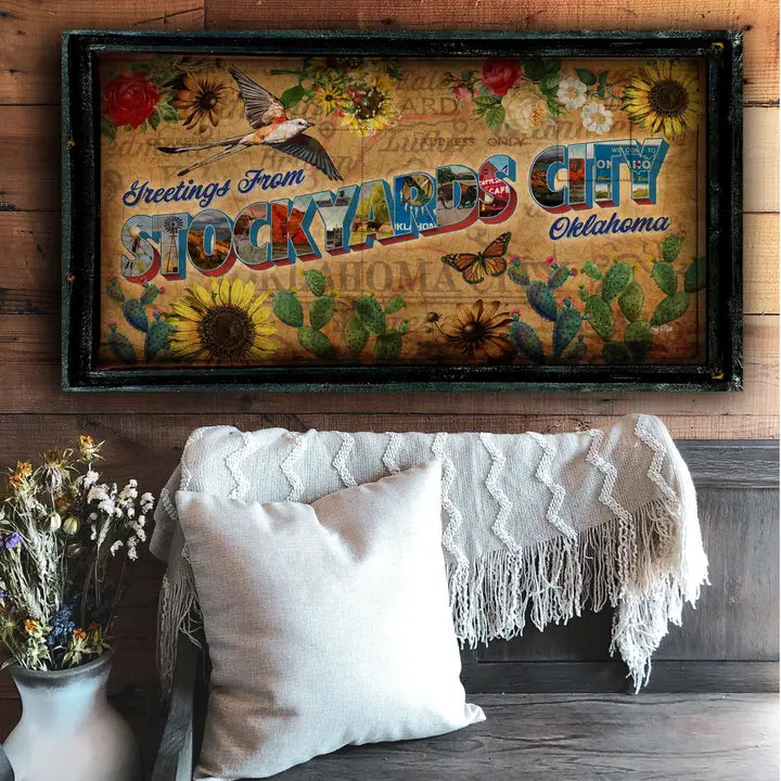Western wall art with 'Greetings from Stockyards City, Oklahoma' on a wooden wall above a couch.