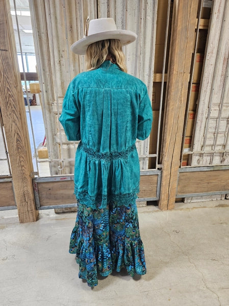 Person wearing a teal jacket with Peacock Feather Boho Pants and a white hat in an indoor setting.
