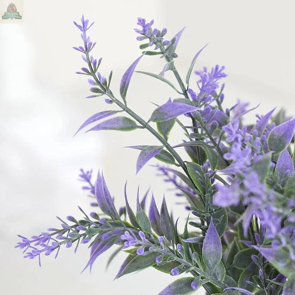 Close-up of a 13" Plastic Lavender Bush featuring green leaves and delicate purple blossoms, made from weather-resistant materials. Case includes 12 bushes, set against a soft background.
