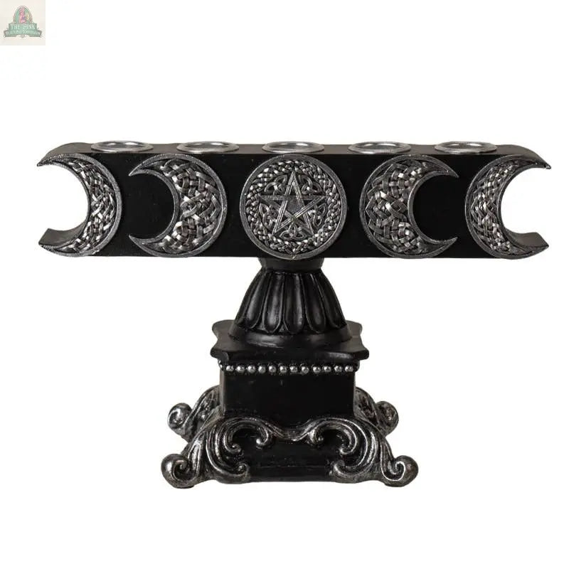 The Triple Moon Candleholder is black cold cast resin with silver crescent moons, a pentagram design, and an ornate base. It holds five candles in a row along the top.