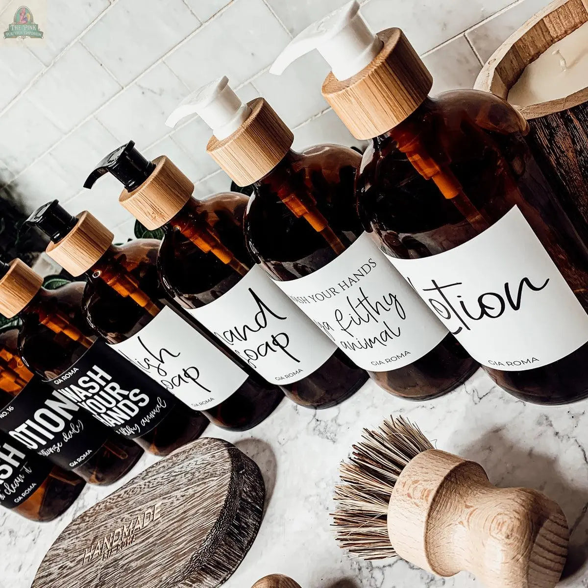 16oz Glass Amber | White Label bottles for dish soap, hand wash, hand soap, and lotion are lined up on a marble countertop, with wooden cleaning brushes and a textured soap dish in the foreground.